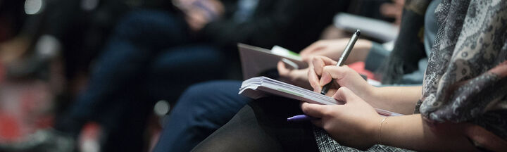 A woman takes notes seated in a row of conference delegates