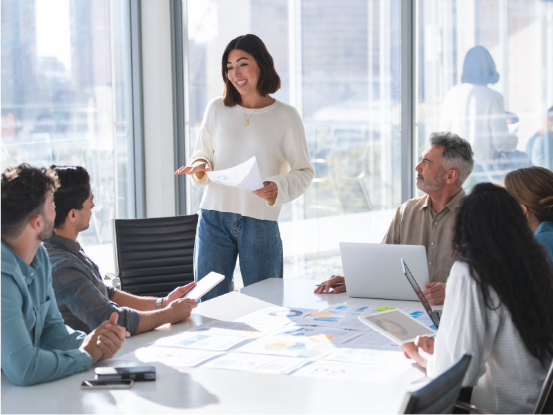 Woman standing in a meeting room addressing a group sat around a table