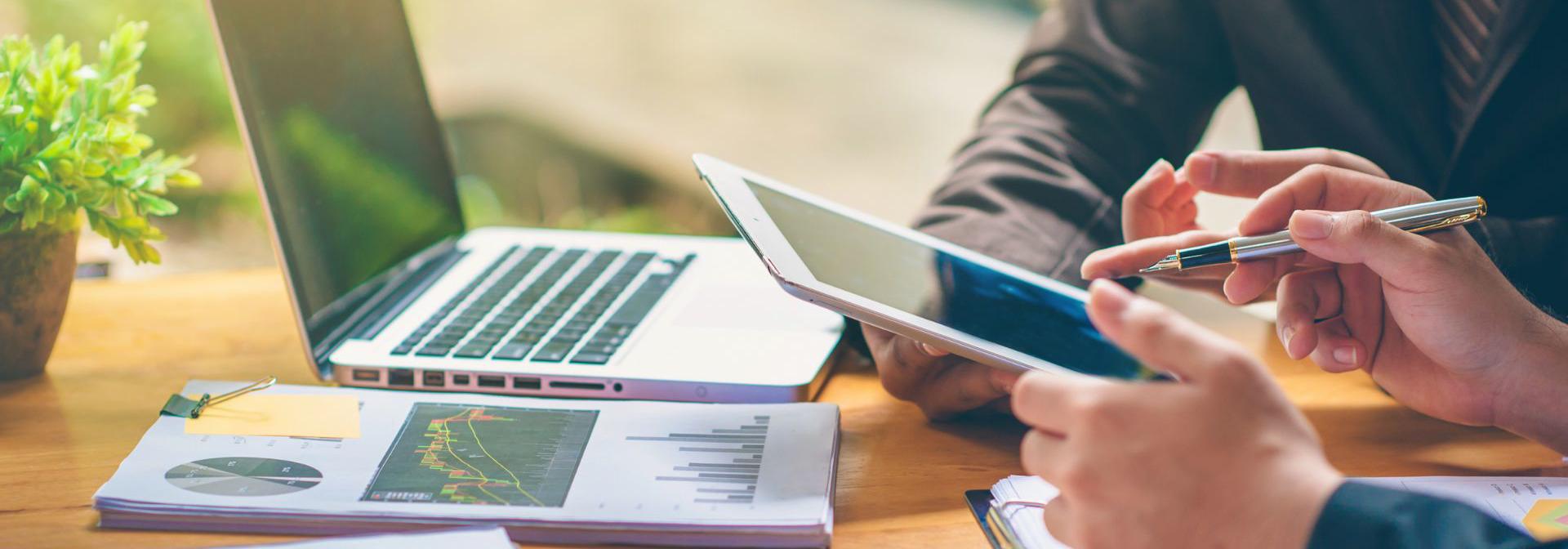 Two people working with a tablet computer, laptop and a series of charts