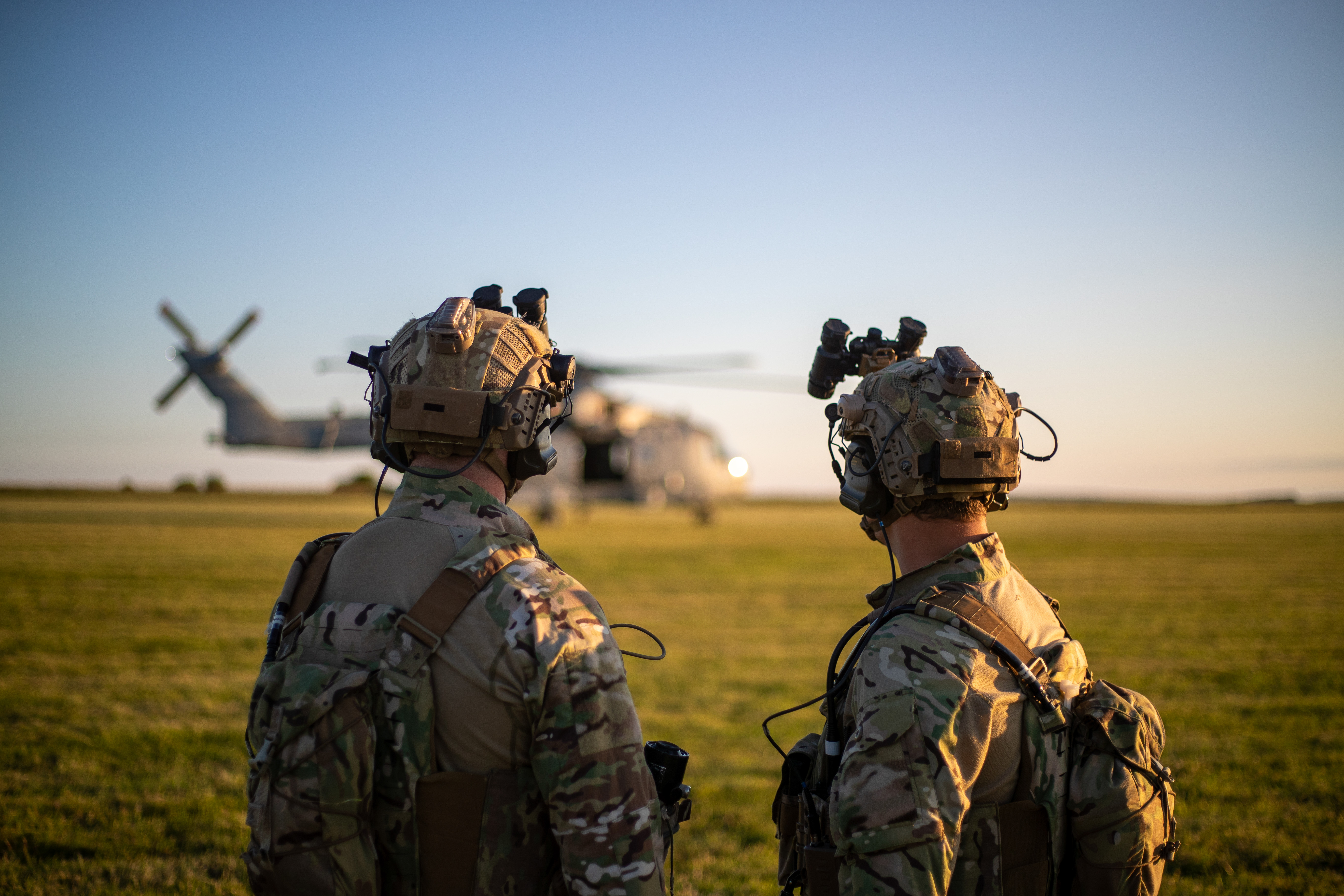 Two armed forces personnel look towards an RAF helicopter during a military exercise