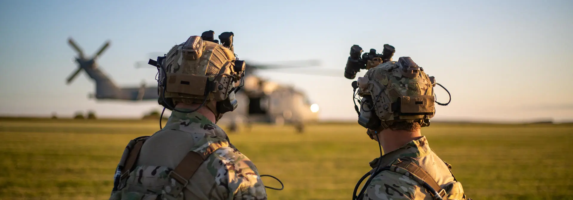 Two armed forces personnel look towards an RAF helicopter during a military exercise
