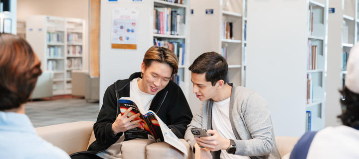 Two students sitting in a library in discussion over a book