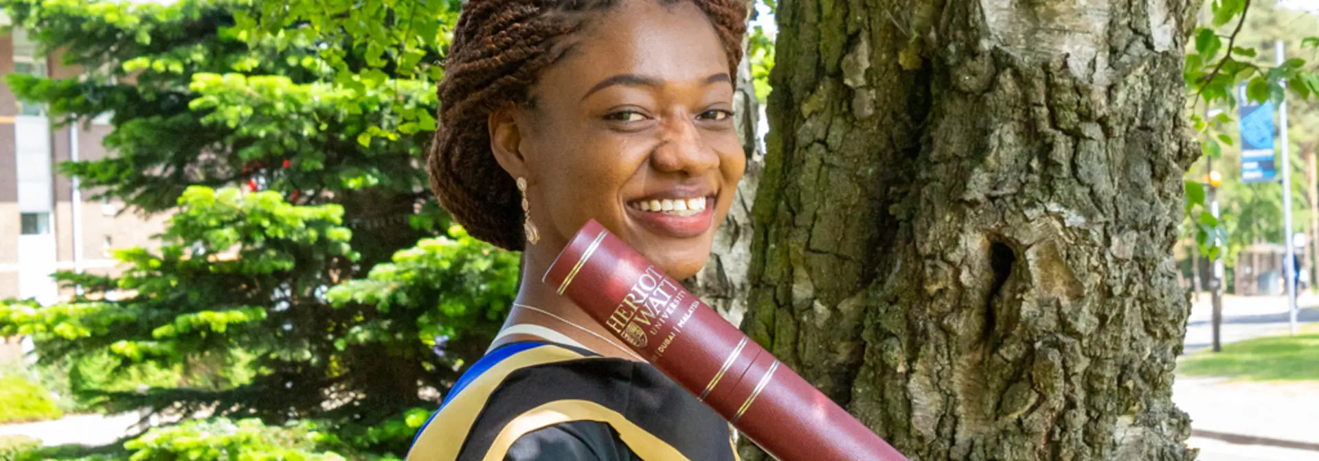 A student wearing the graduation robes and holding a scroll