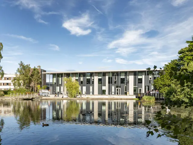 The GRID building stands behind a serene Loch, reflecting its structure in the calm water.