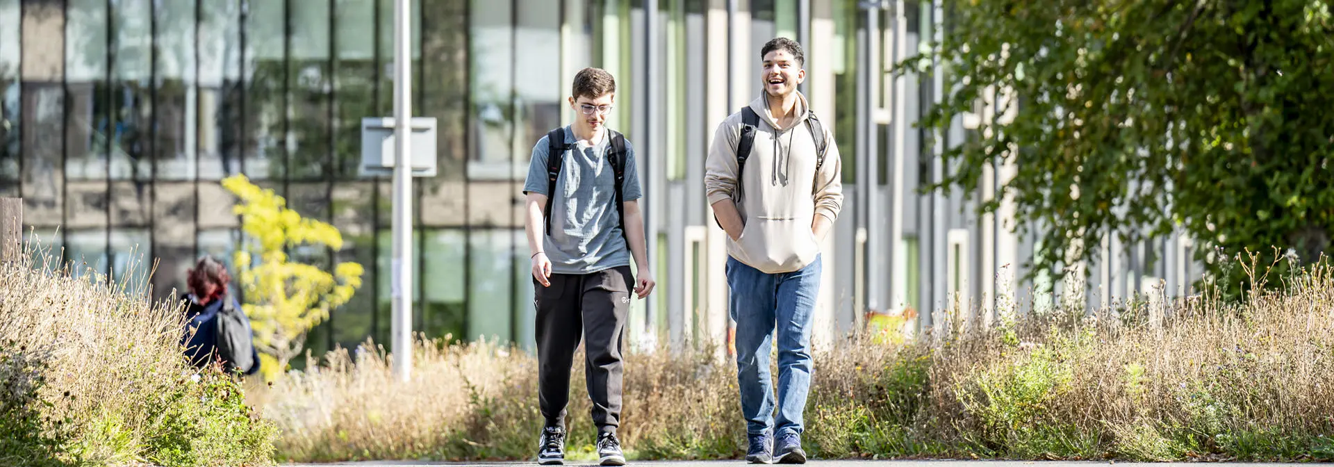 Two students walking and talking on a sunny paved path near the GRID building.