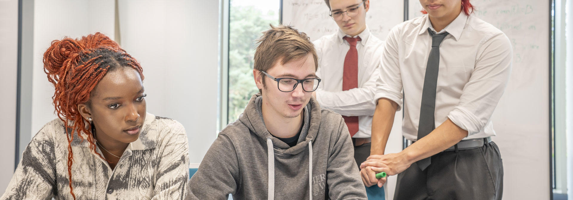 Four students collaborate on a laptop in a modern office setting, focused on their work and sharing ideas.