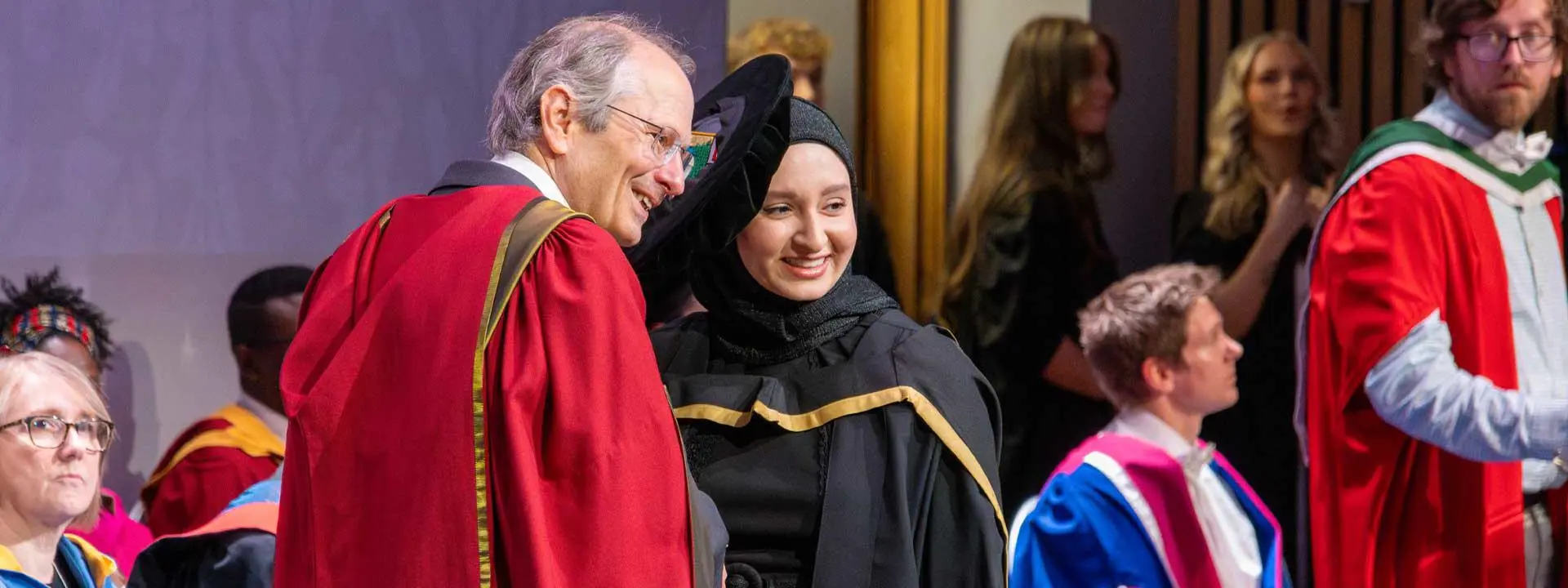 A woman and a man wear graduation gowns, smiling proudly as they commemorate their graduation day.