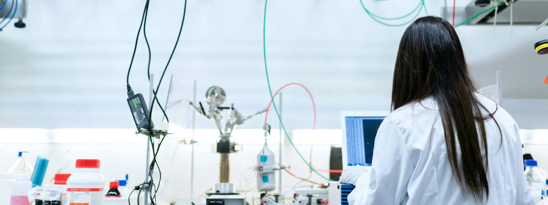 A woman in a lab coat is focused on her work while using a computer in a laboratory setting.