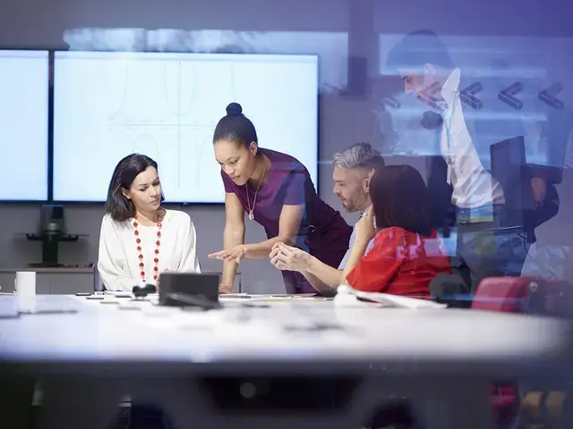 A woman leads a group of people in review of documents on the table.