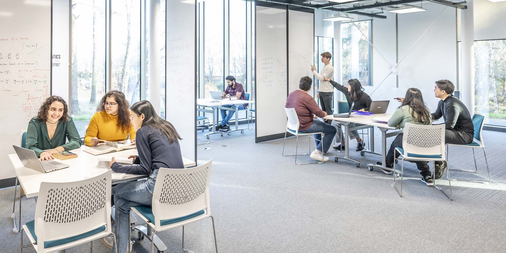 Students collaborate on projects in a bright study space with white walls and large windows.