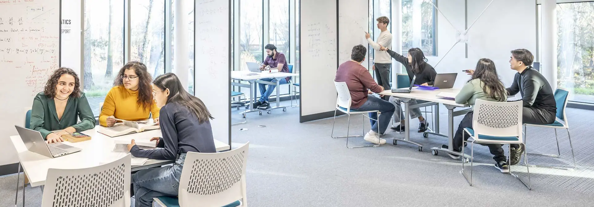 Students collaborate on projects in a bright study space with white walls and large windows.