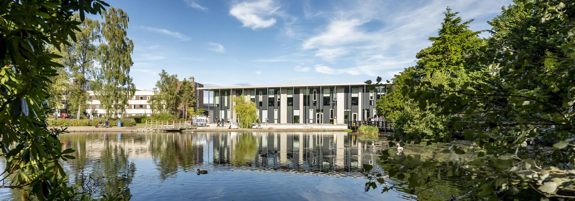 The modern GRID building reflecting in a serene Loch, surrounded by lush trees and clear blue skies.