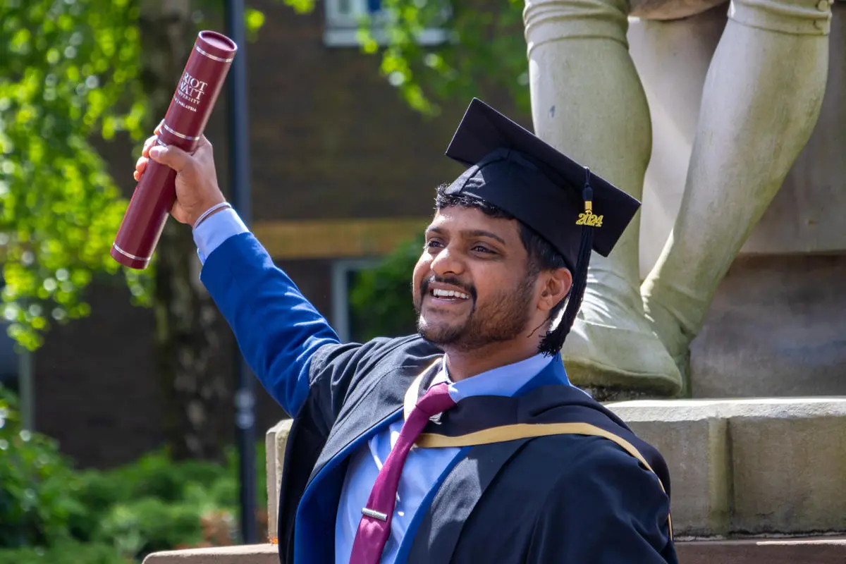 A man holds up a certificate holder on graduation day
