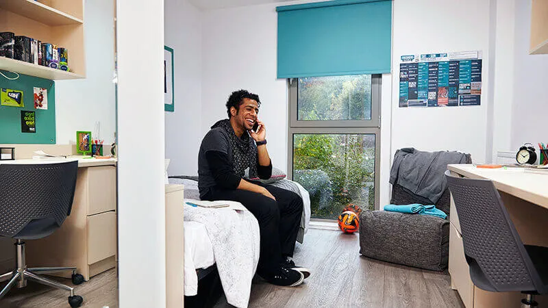 Student sitting on bed making phone call