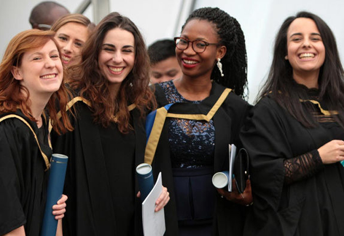 Graduates in gowns holding degrees and smiling
