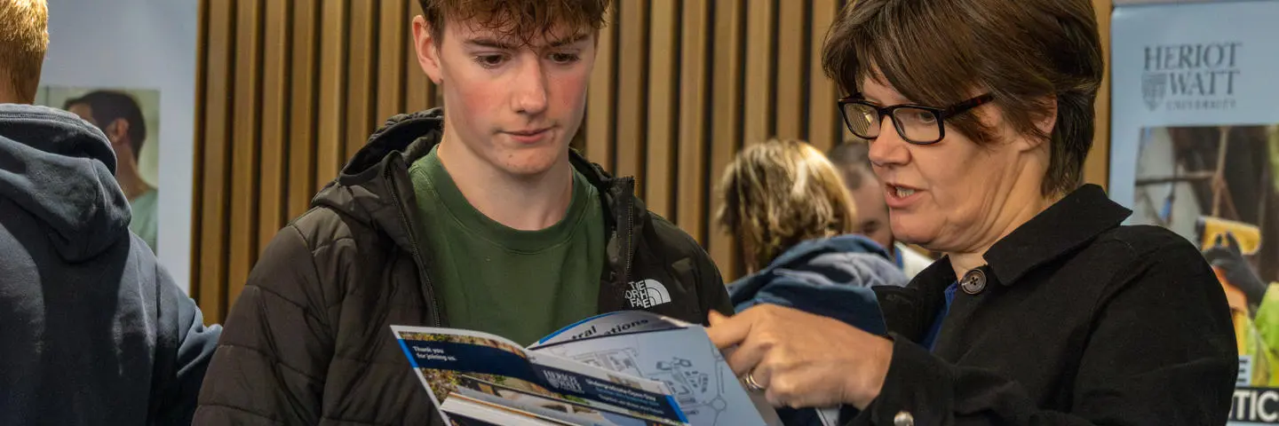 A woman discusses a Heriot-Watt prospectus with a young man