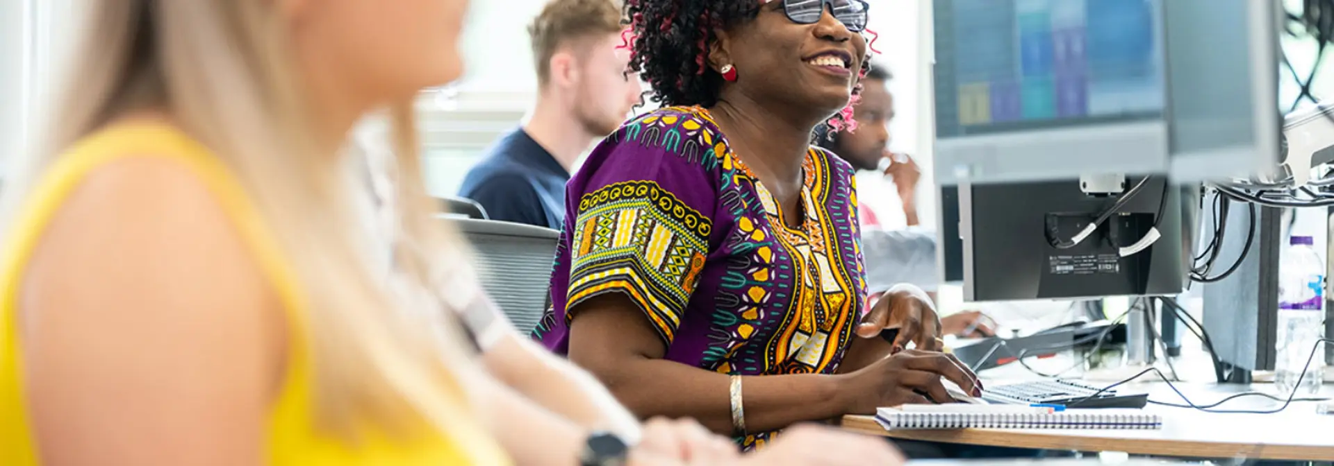 A smiling woman works at a desk and on a computer in an office.