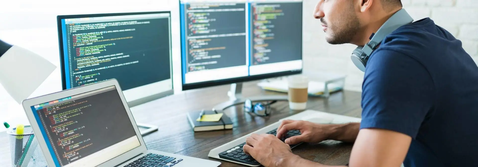 An individual working across three screens on code.