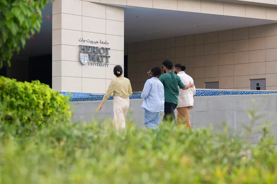 Four students walking towards the Heriot-Watt University Dubai campus entrance.