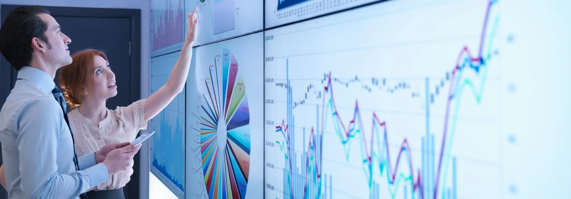 Two individuals discussing and reviewing graphs on a board.