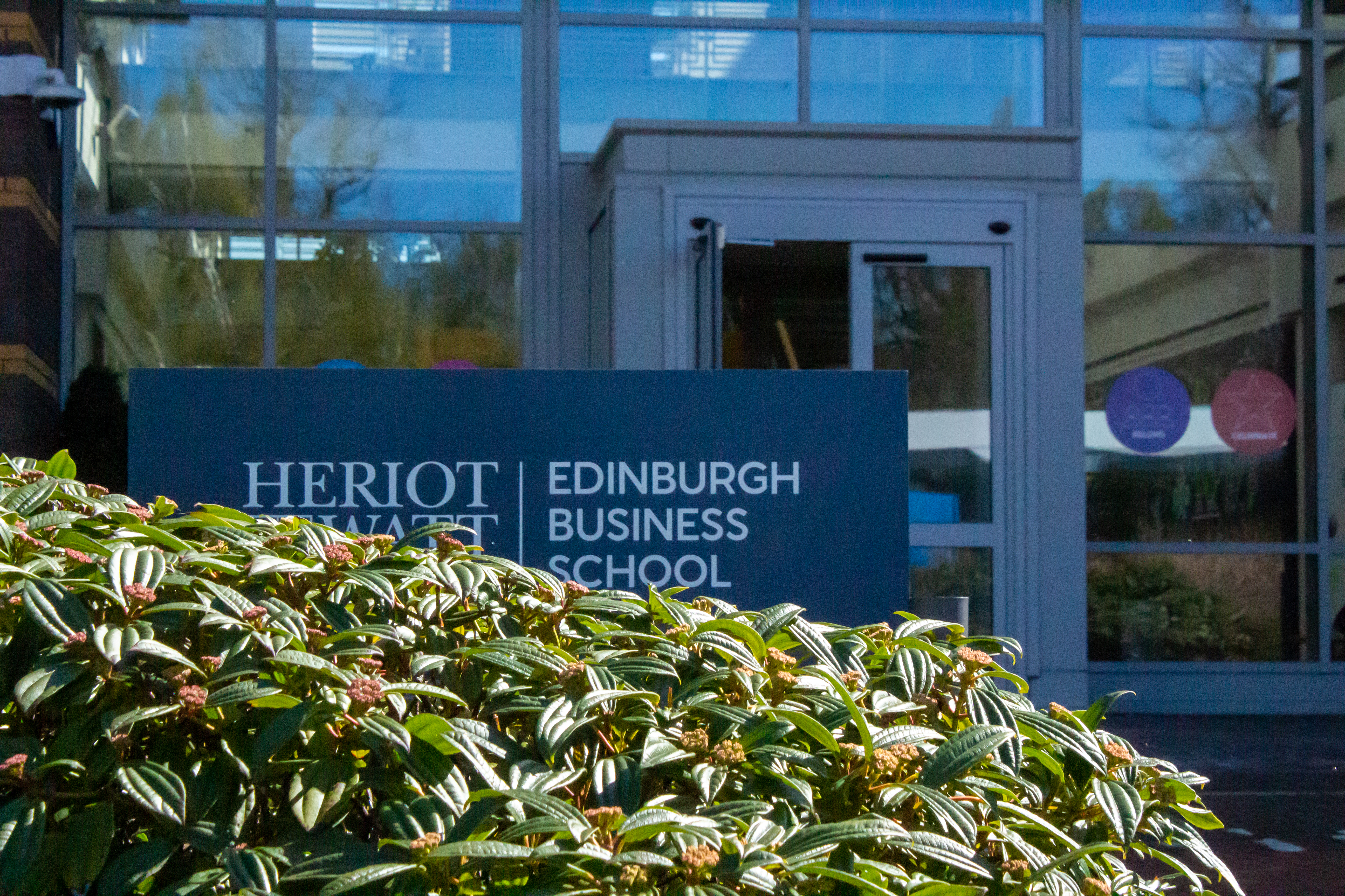 A leafy bush in front of the Heriot-Watt Edinburgh Business School entrance and sign.