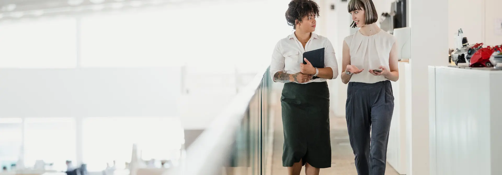 Two woman walk through a corridor in conversation.
