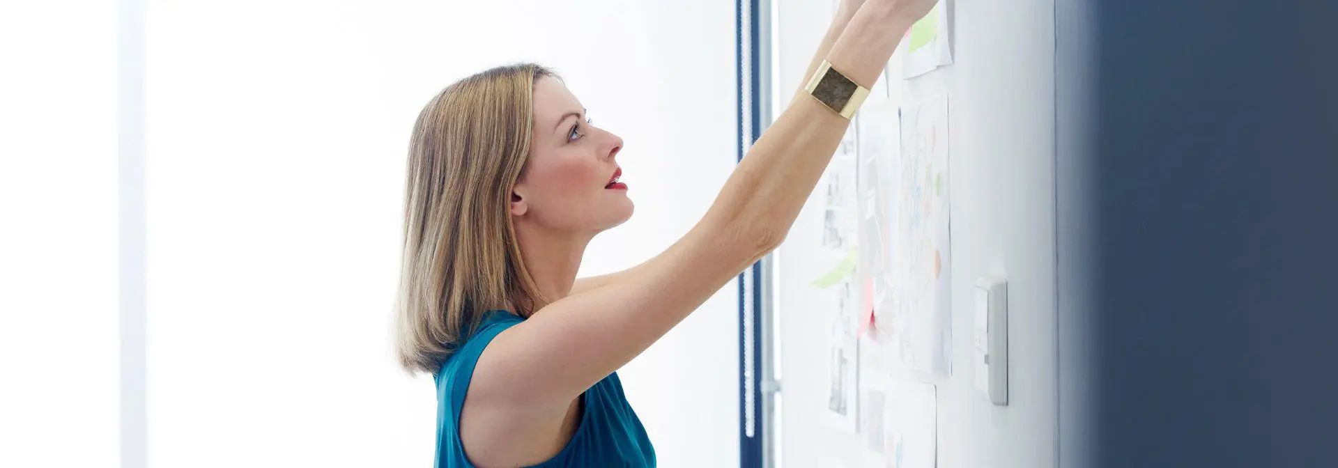 Woman pins paper to a board in a meeting room.