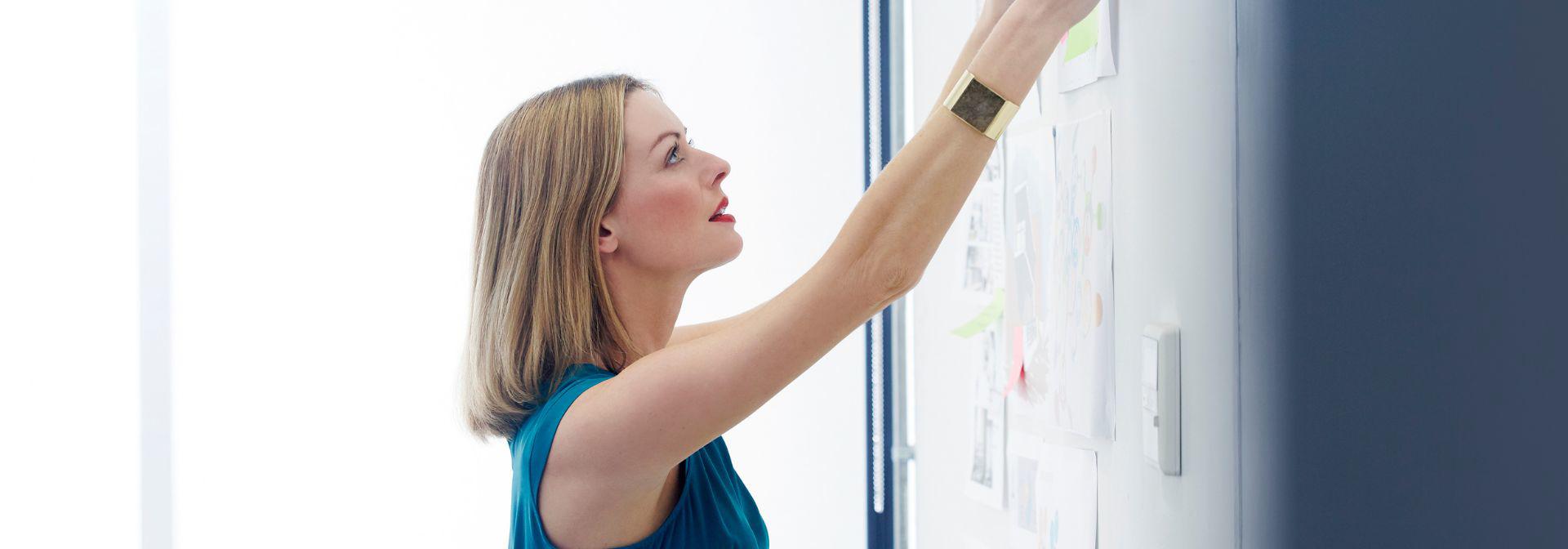 Woman pins paper to a board in a meeting room.