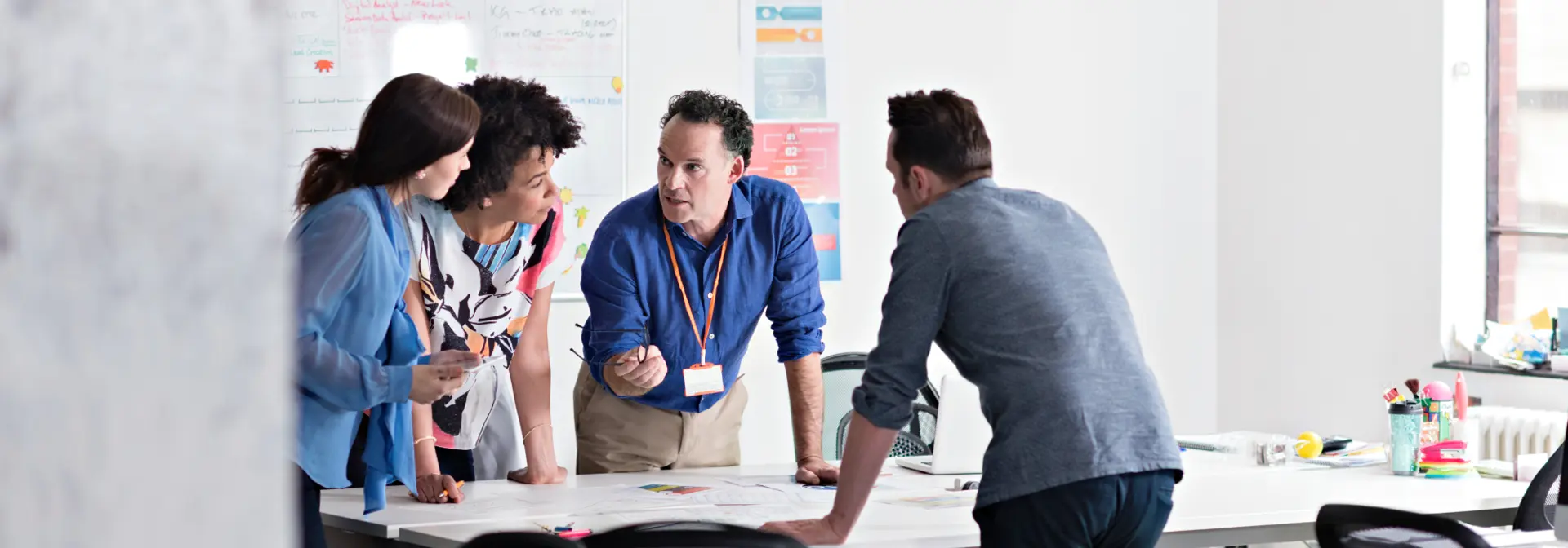 Four individuals lean over a table discussing a project intently.