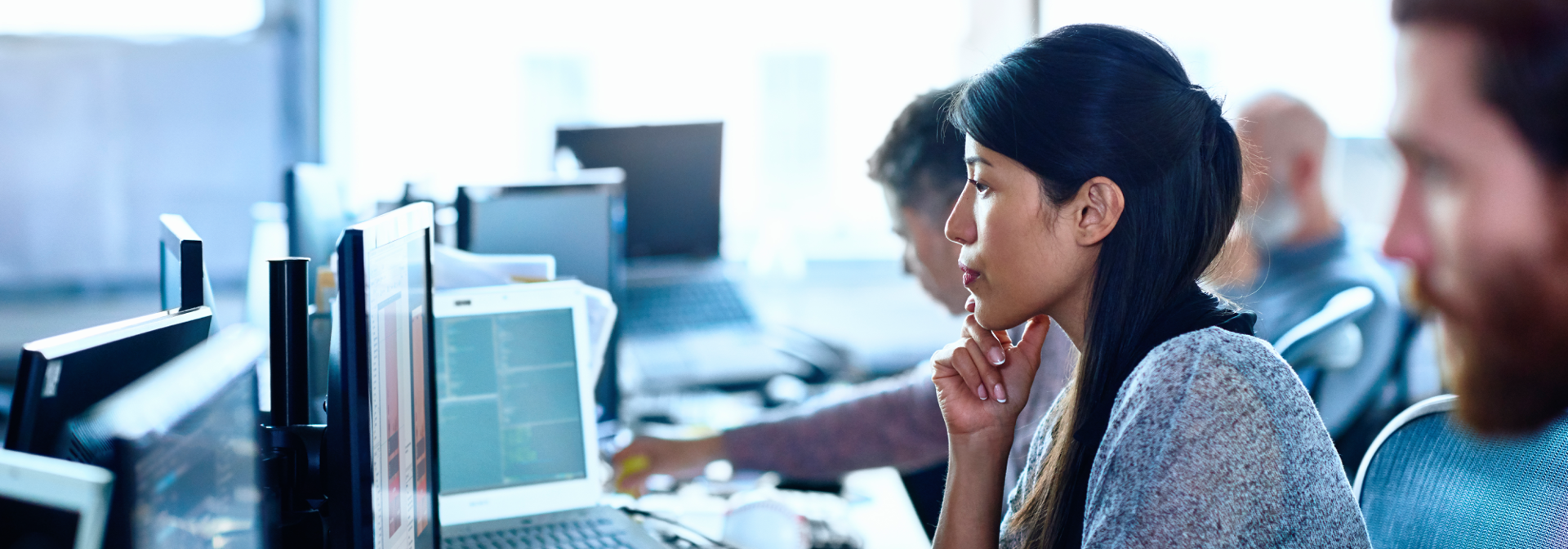 A woman leans forward at a desk focused on her computer screen.