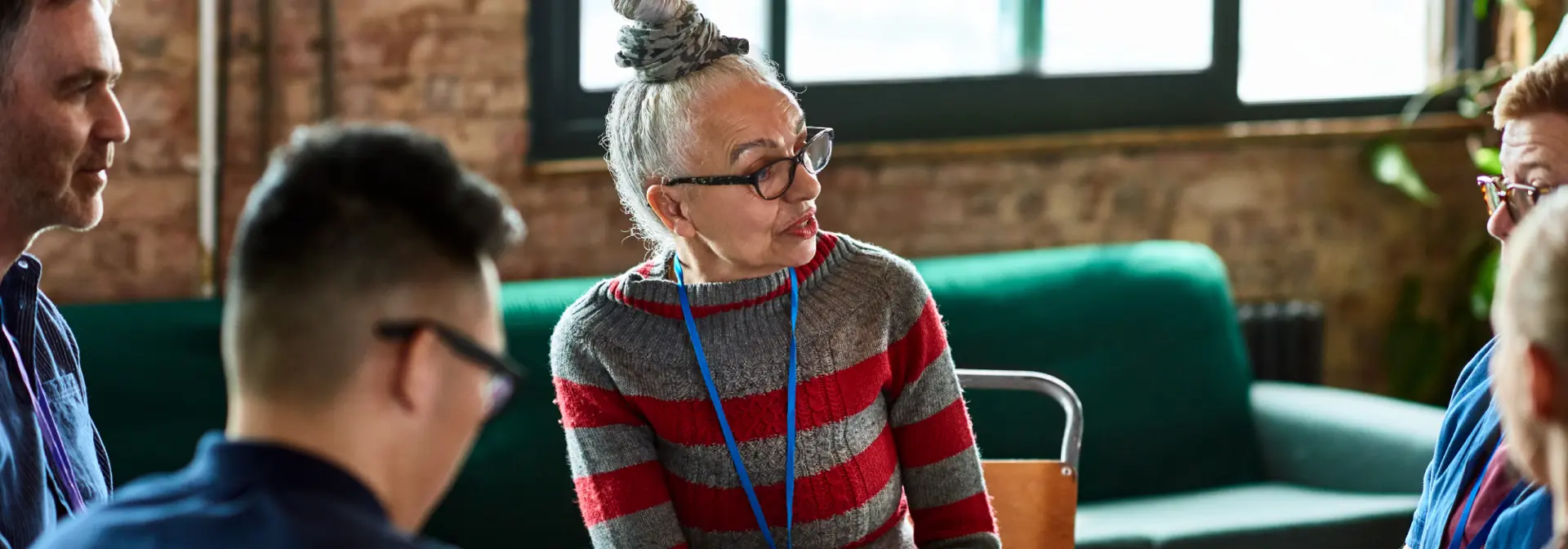 A woman with her hair in a bun sits and speaks in a focus group of individuals.
