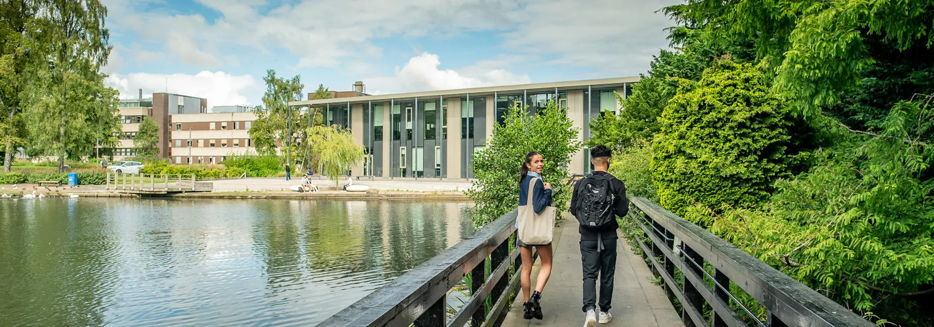 Two students walking across a bridge over a loch.