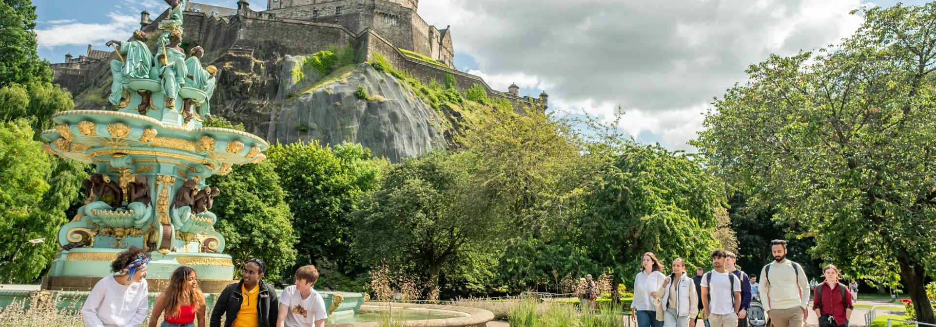 Students walking through Princes Street Gardens in Edinburgh on a sunny day with the castle in background.
