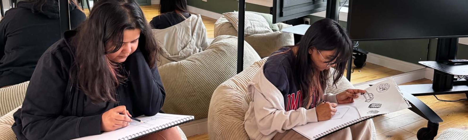 Two students sitting and drawing on sketch pads.