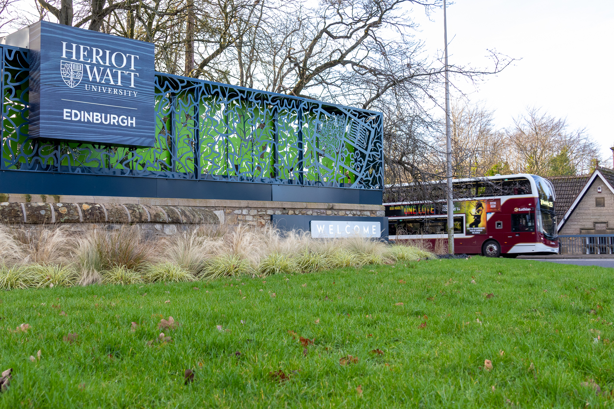 An entrance sign for Heriot-Watt University with a bus driving in the background.