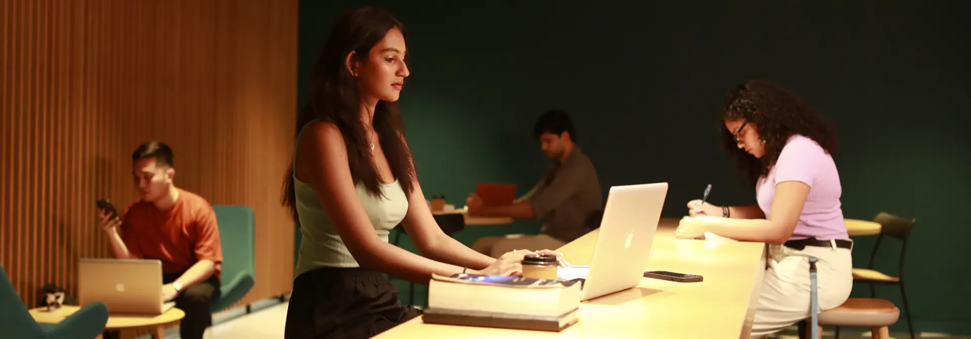 Students sitting in a cafe studying with laptops and writing notes.