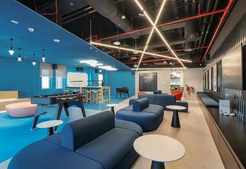 room with black, white and blue walls with blue sofas, foosball tables and TVs