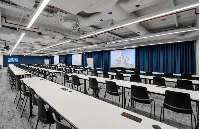 rows of continuous desk with black chairs facing blue curtains
