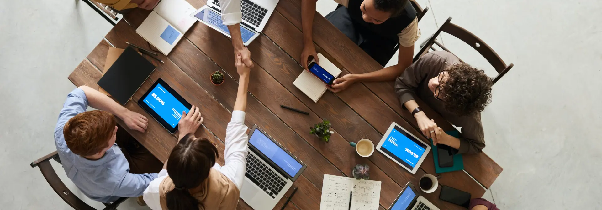 A birds-eye view of two people shaking hands over a table at a meeting.
