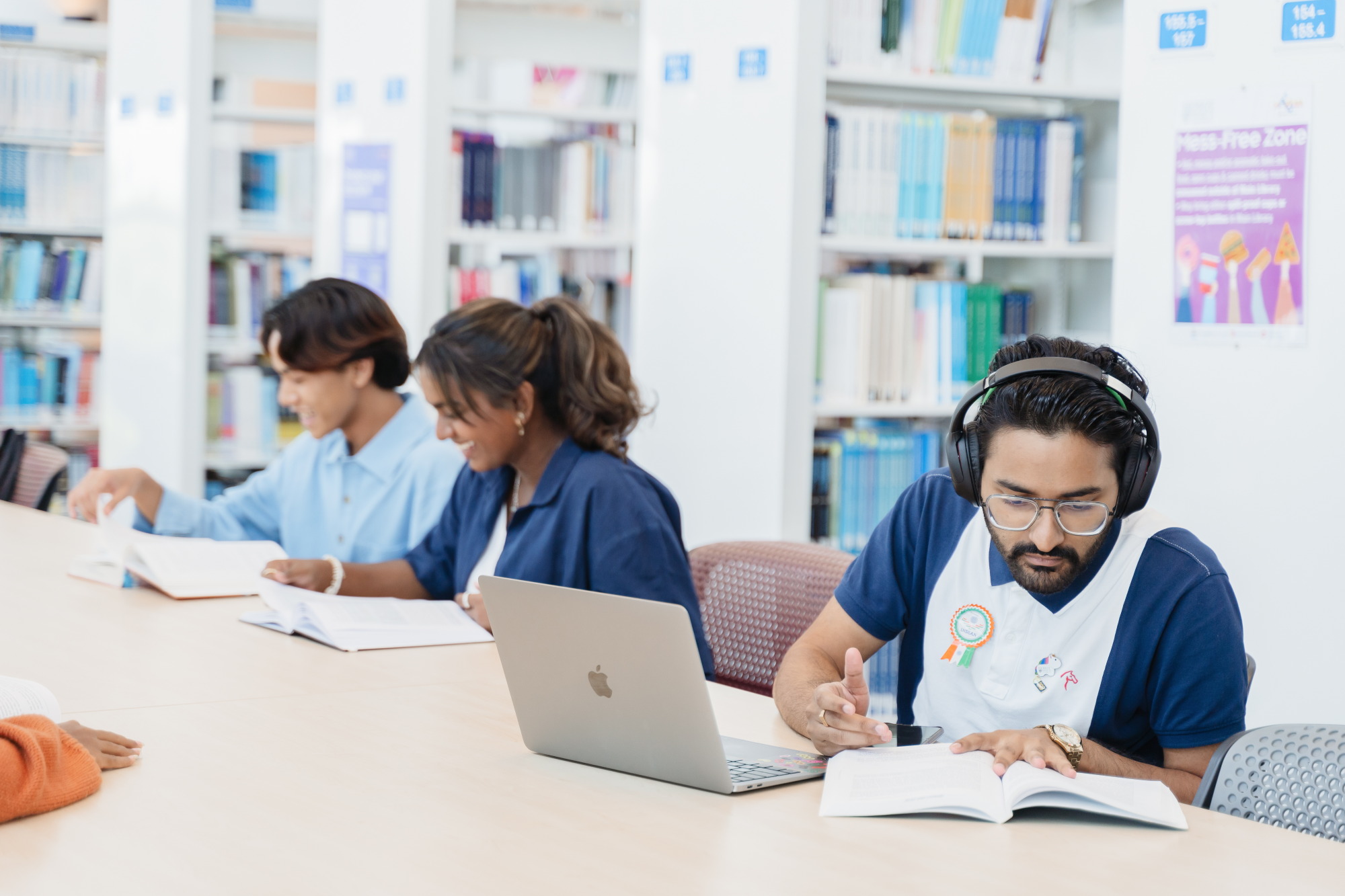 Three individuals work in a library with books and a laptop.