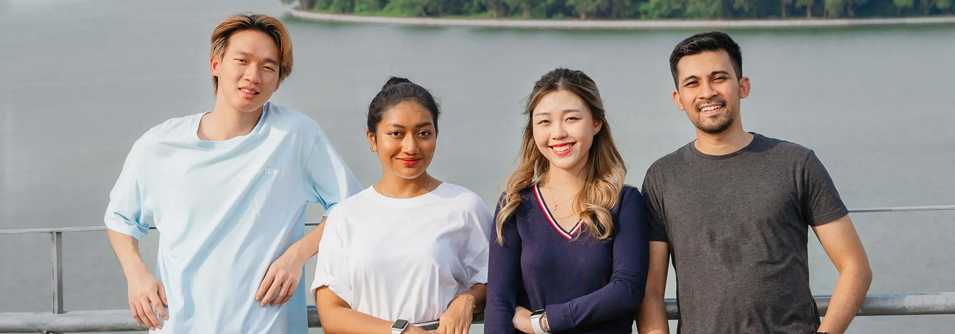 Four students standing together by a fence with a lake behind them.