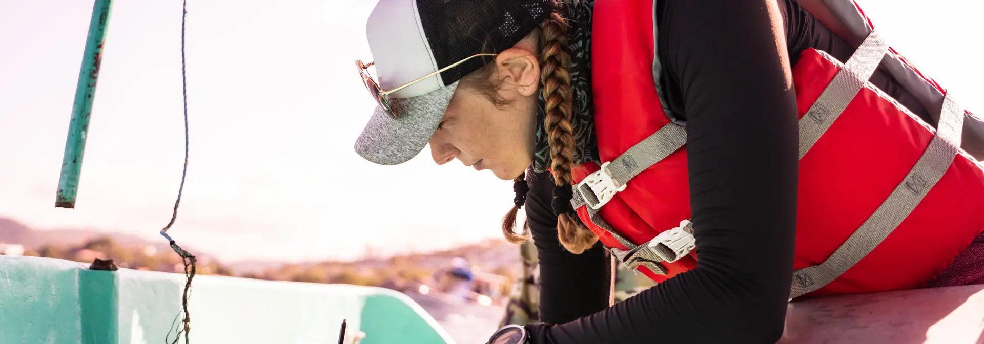 A student wearing a life jacket is on a boat writing notes.