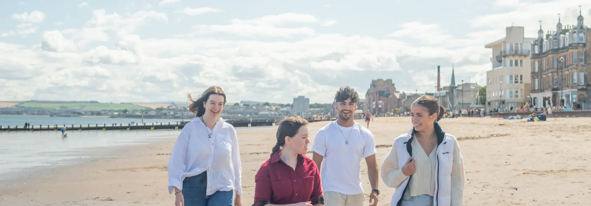 Four individuals walking across a beach with a town in the background.