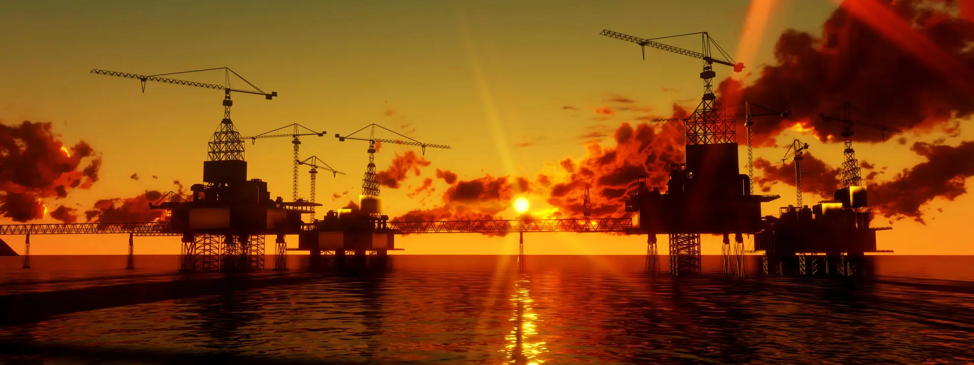 Silhouetted oil rigs at sea during sunset with cranes