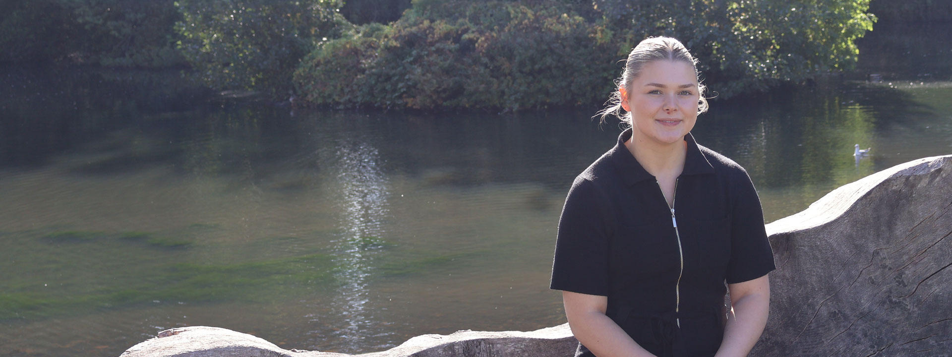 Beth A smiling in the sunshine in front of the Edinburgh Campus loch.