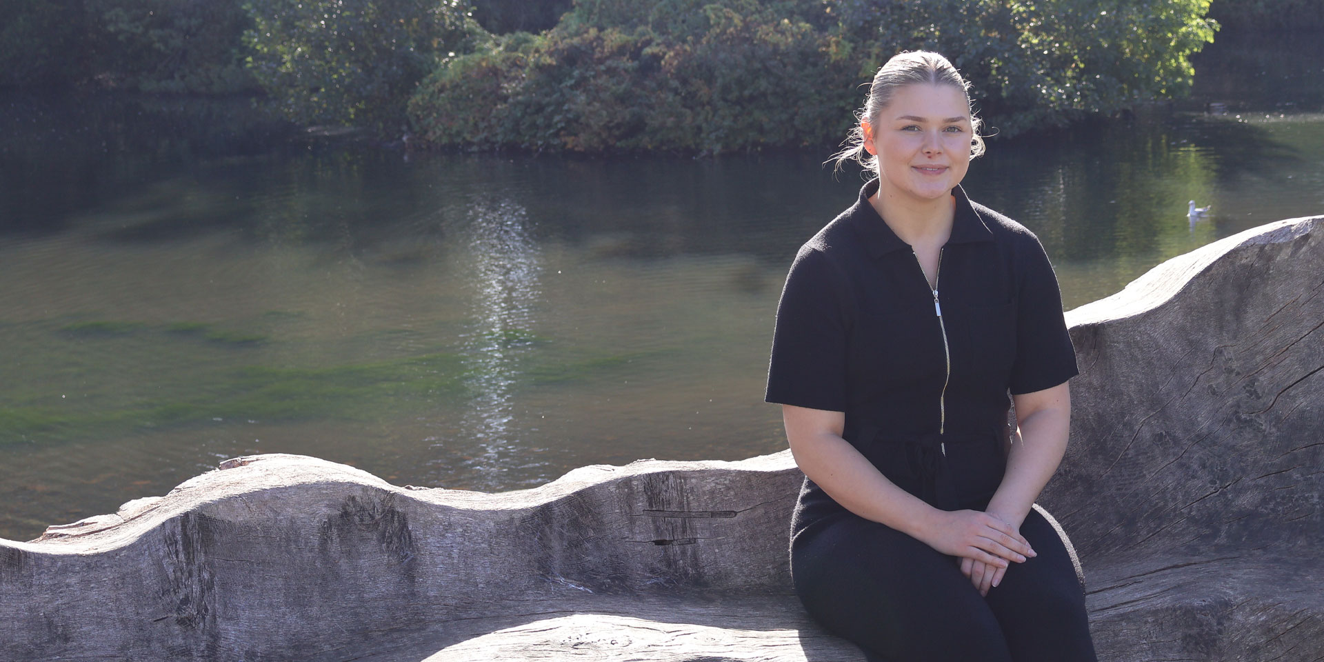 Beth A smiling in the sunshine in front of the Edinburgh Campus loch.
