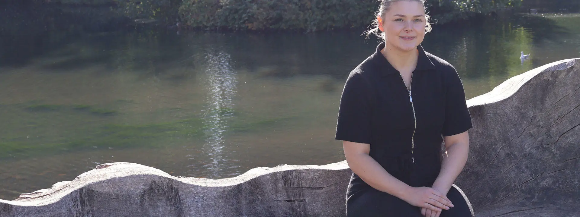 Beth A smiling in the sunshine in front of the Edinburgh Campus loch.