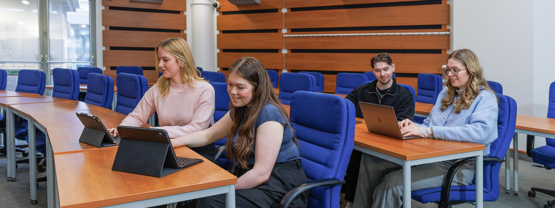 Students seated in a conference room using laptops and tablets.
