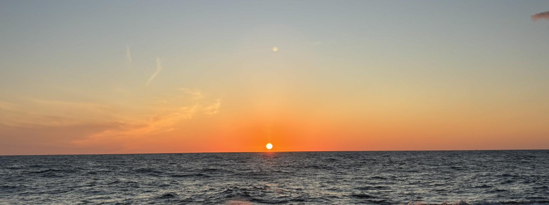 The image shows a beautiful sunset over the ocean. The sun is partially below the horizon.