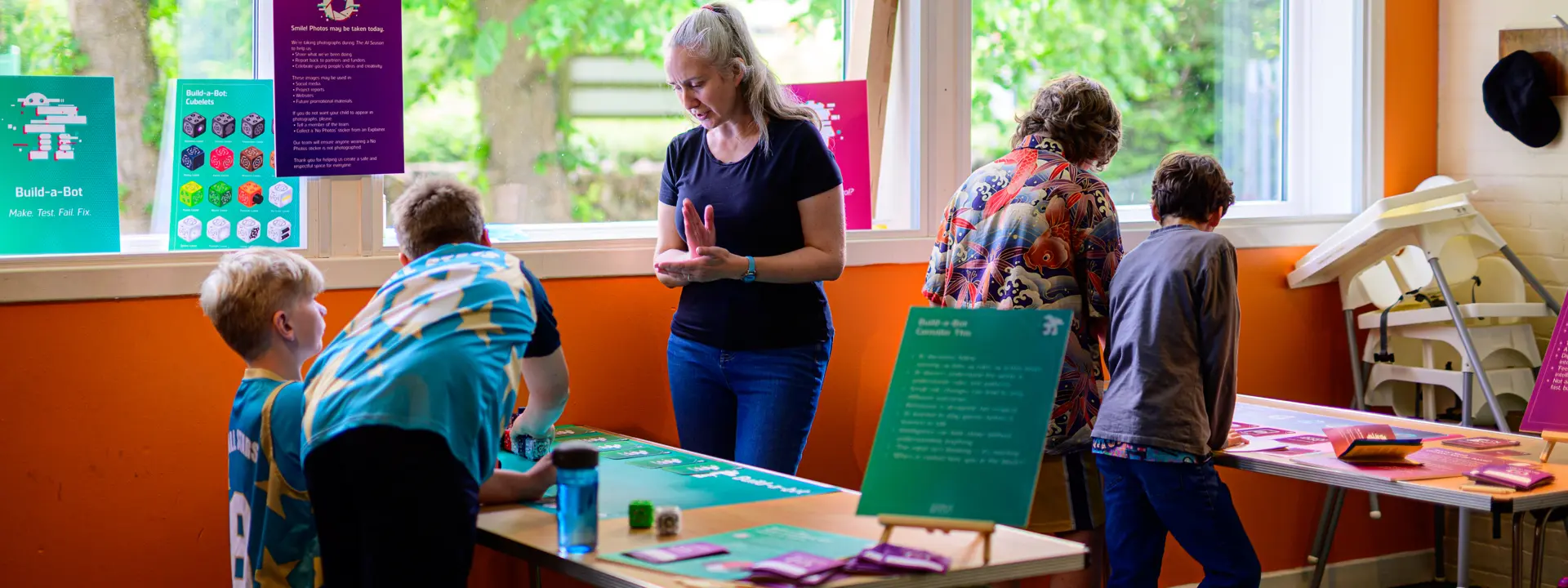 A group of children supervised by adults gathered around the tables with colourful leaflets